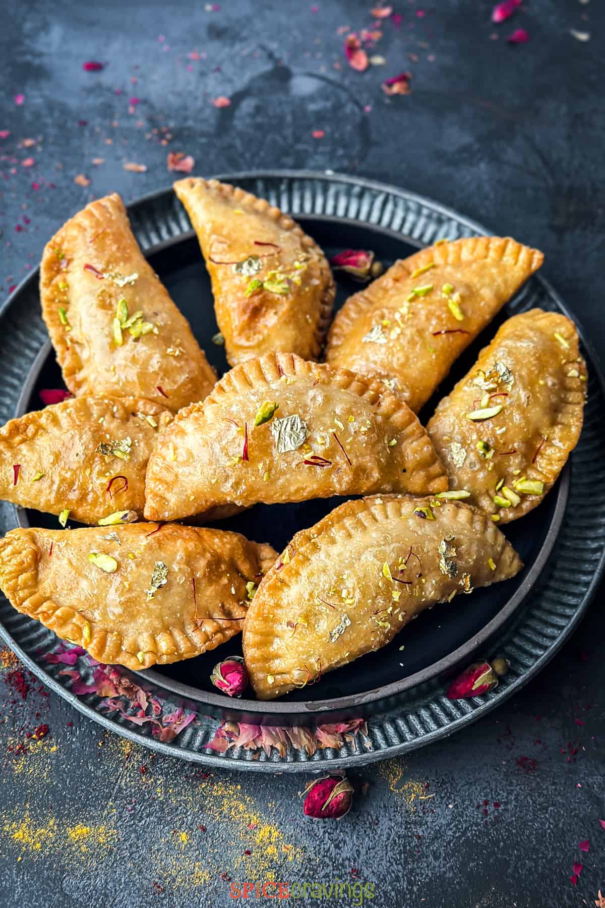 Gujiya garnished with pistachio, saffron and gold foil placed on metal trays