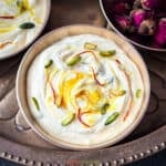 close up of shrikhand in copper bowl garnished with pistachio and saffron