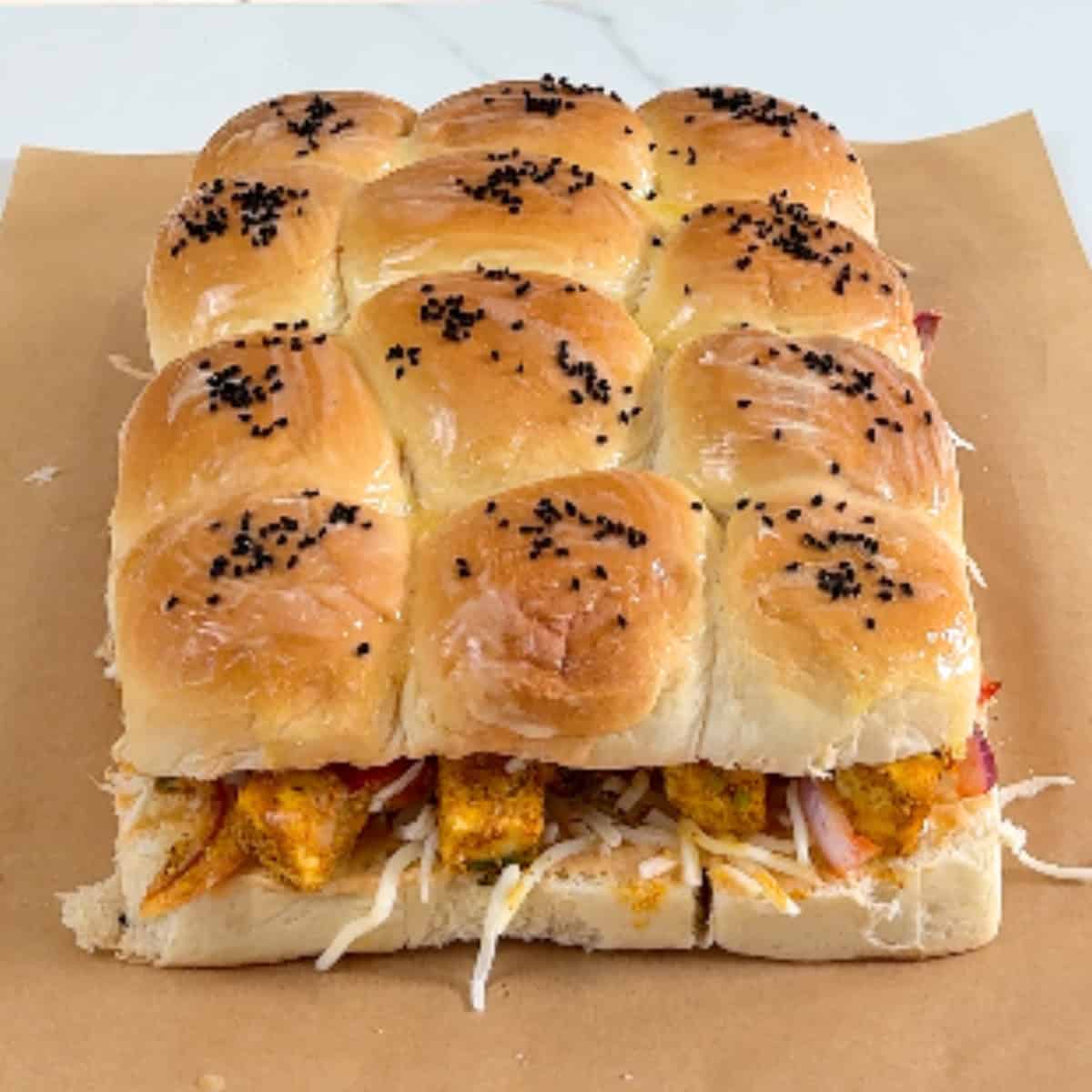 Set of 12 sliders on parchment paper, sprinkled on top with black onion seeds