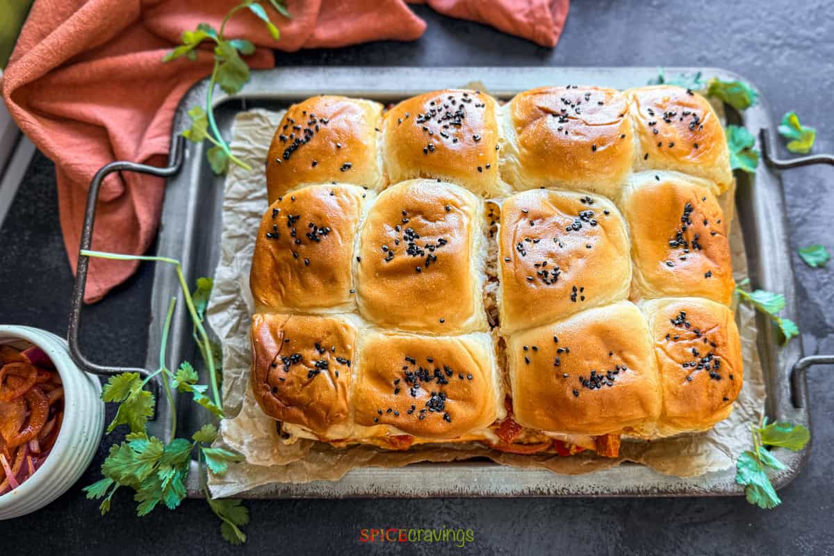 A metal tray with paneer tikka sliders, cilantro and pickled onions on the side.