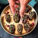 Hand holding a single stuffed date paan against a background of a brass plate with dates paan and dried rose buds