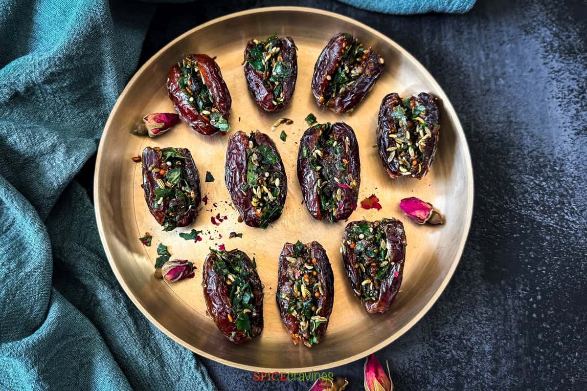 A brass plate with stuffed date paan with betel leaves, fennel, gulkand, fennel and dried rose