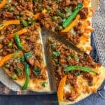A wedge of keema naan pizza topped with bell peppers and indian ground meat called keema