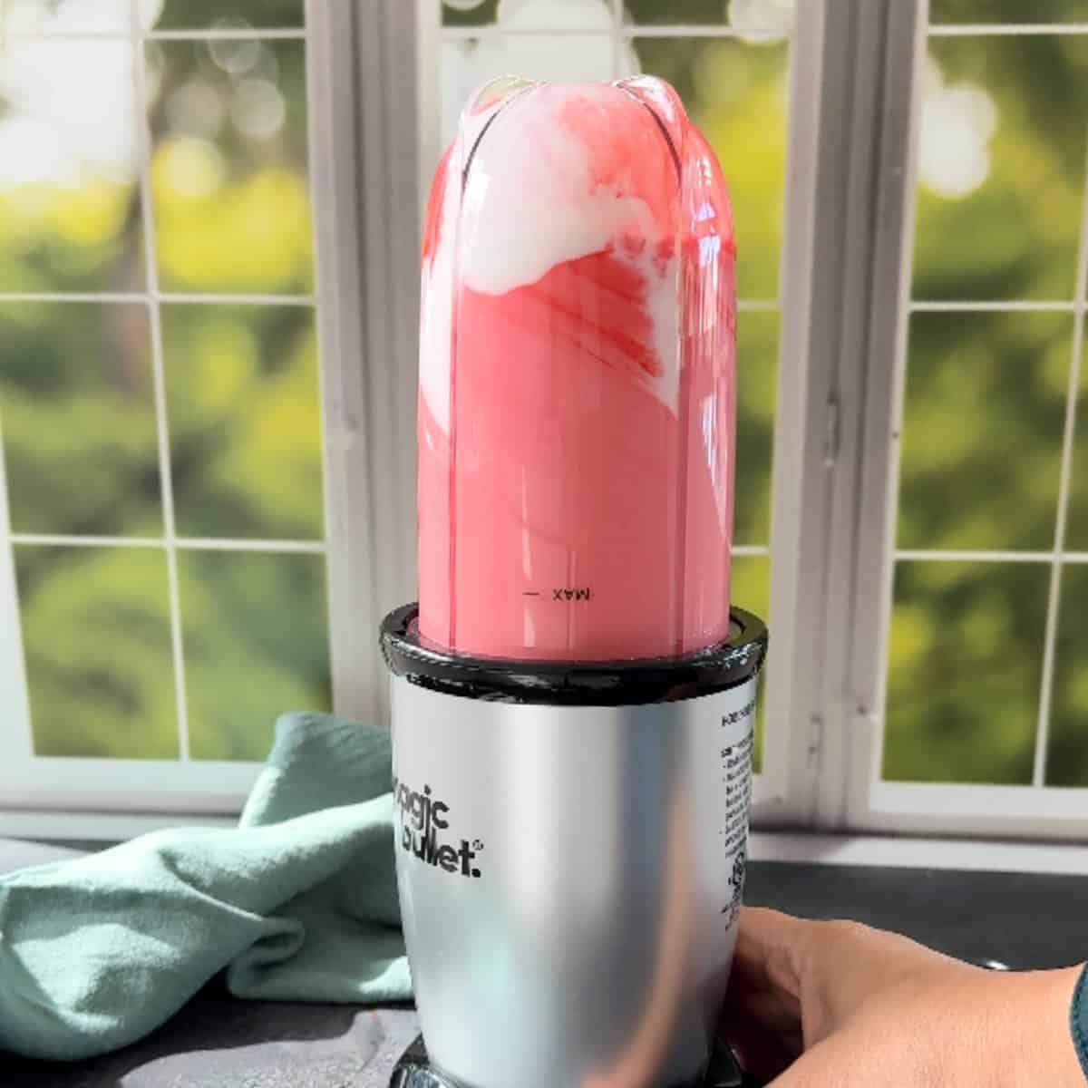 Pink colored Rose Lassi made with yogurt, rose, syrup and cardamom in a small blender
