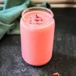 A single glass filled with vibrant pink rose lassi, a popular Indian yogurt smoothie made with yogurt, rose syrup and cardamom