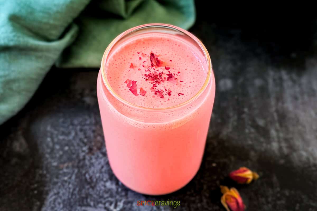 A single glass filled with vibrant pink rose lassi, a popular Indian yogurt smoothie made with yogurt, rose syrup and cardamom