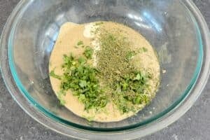 A glass bowl containing the base for Malai Tikka marinade with heavy cream, yogurt, fresh cilantro, and dried fenugreek leaves (kasuri methi)