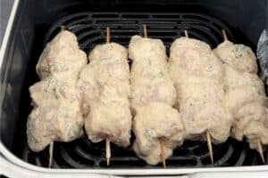 Raw marinated chicken skewers placed in a single layer inside a black air fryer basket.