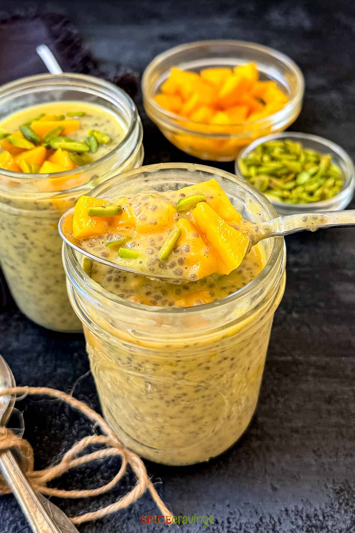 Spoonful of mango pudding with chia seeds and pistachio in a glass jar