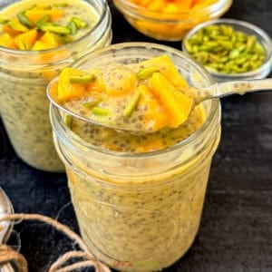 Spoonful of mango pudding with chia seeds and pistachio in a glass jar