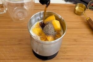 Adding maple syrup to a blender jar with mango, milk and cardamom for a quick chia and mango pudding