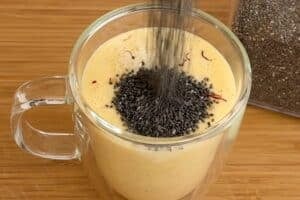 Adding chia seeds and saffron strands to a glass cup with mango and chia pudding
