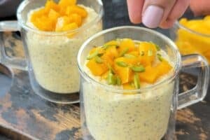 sprinkling pistachio slices in a cup with chopped mango and overnight oats