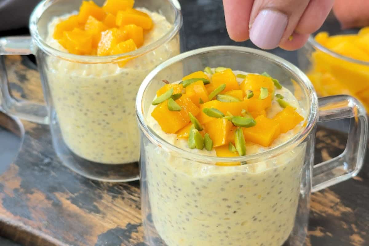 sprinkling pistachio slices in a cup with chopped mango and overnight oats