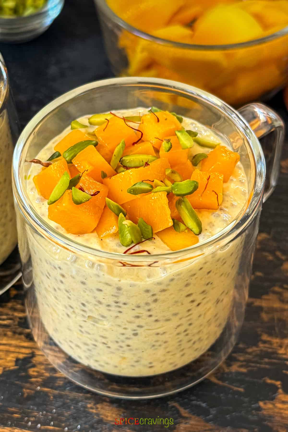 cup of mango overnight oats with chia seeds topped with chopped mango and pistachios