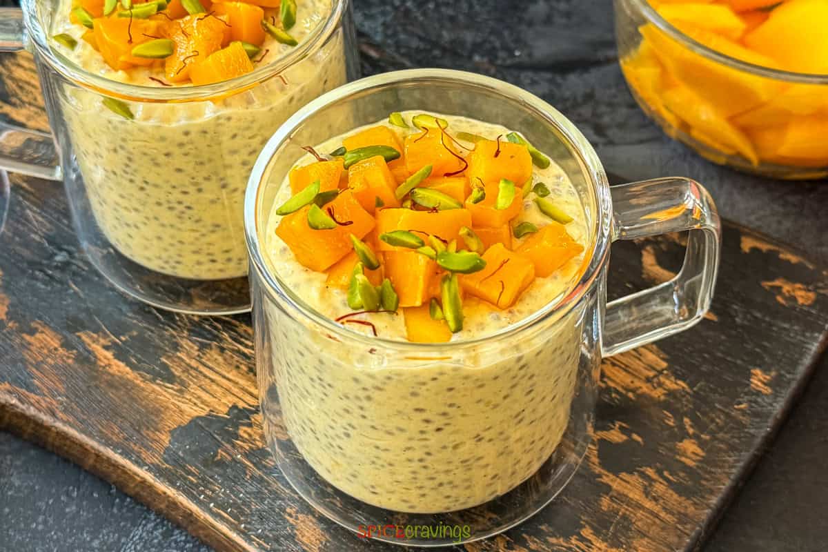 two cups of mango overnight oats with chia seeds topped with chopped mango and pistachios