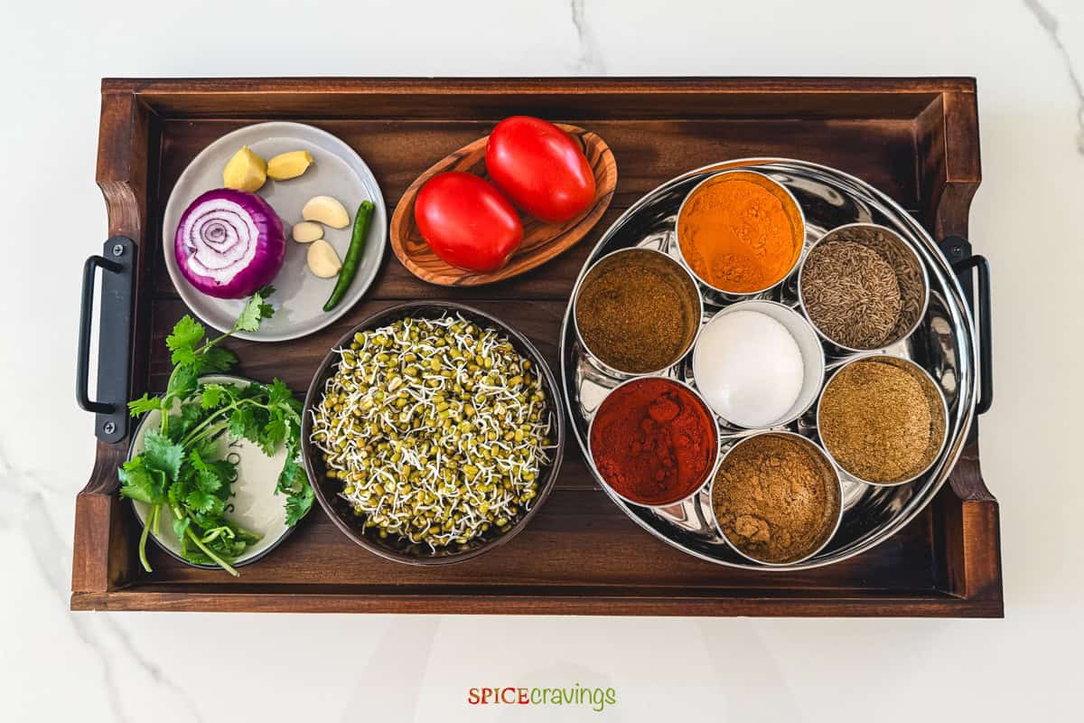 Assorted spices, herbs, and vegetables on a wooden tray for making sprouts curry