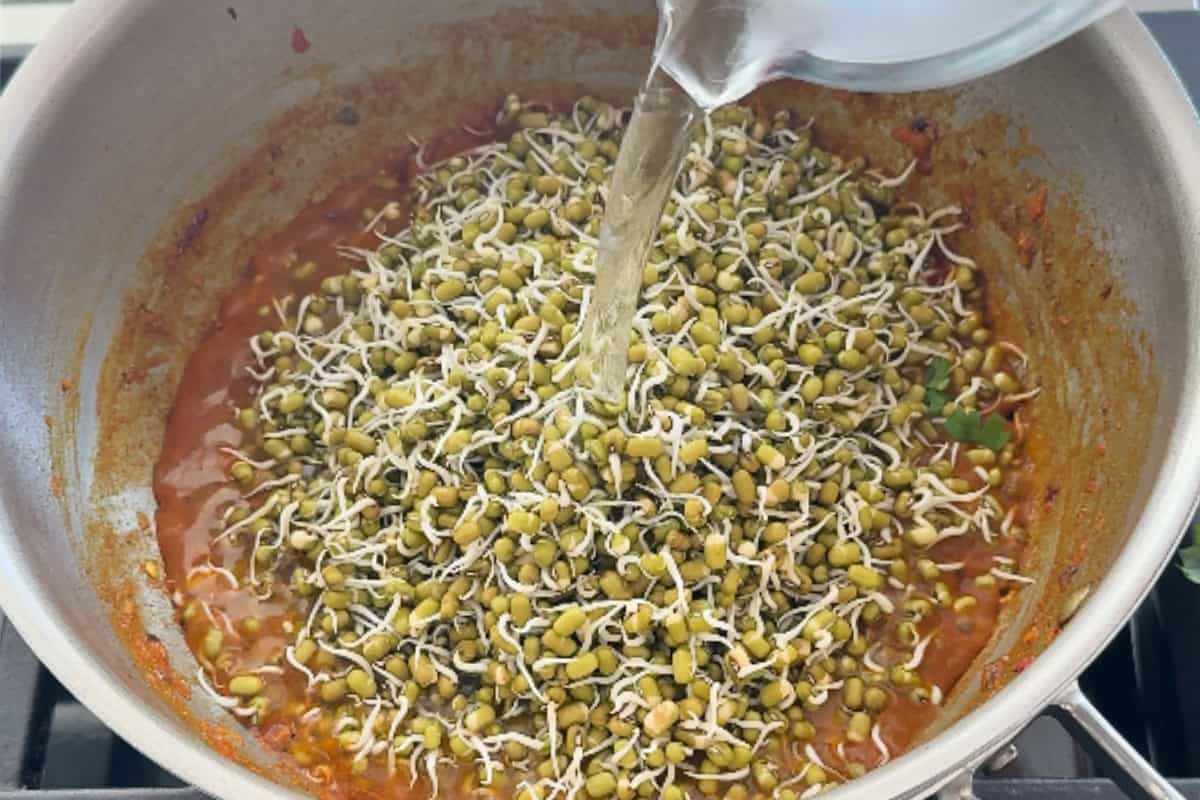 pouring water over moong sprouts and curry mixture in a pan